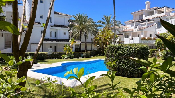 A swimming pool surrounded by well-maintained grass and palm trees, with white buildings in the background. - Spacious Poolside 3 Bedroom F-5 (Marbella)