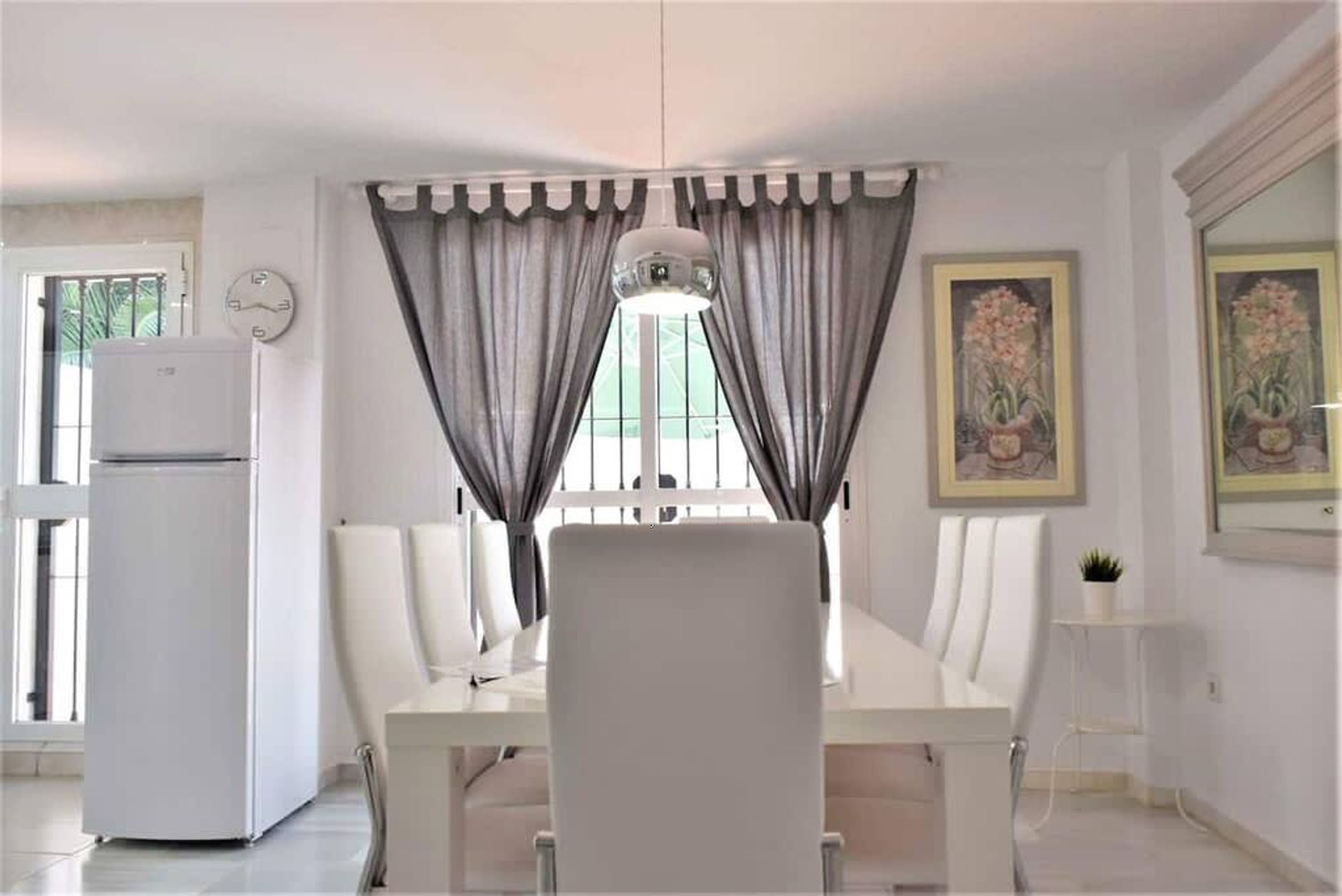 A dining area with a white table, chairs, and a hanging light fixture.