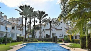 A swimming pool surrounded by palm trees and a white building with balconies. - Villa Emma 4 Bedrooms F-3 (Marbella)