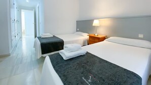 Habitación de hotel con dos camas, una mesita de noche con lámpara y un baño visible a través de una puerta abierta.