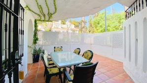 Un patio al aire libre con una mesa y sillas, rodeado por una valla blanca y follaje.