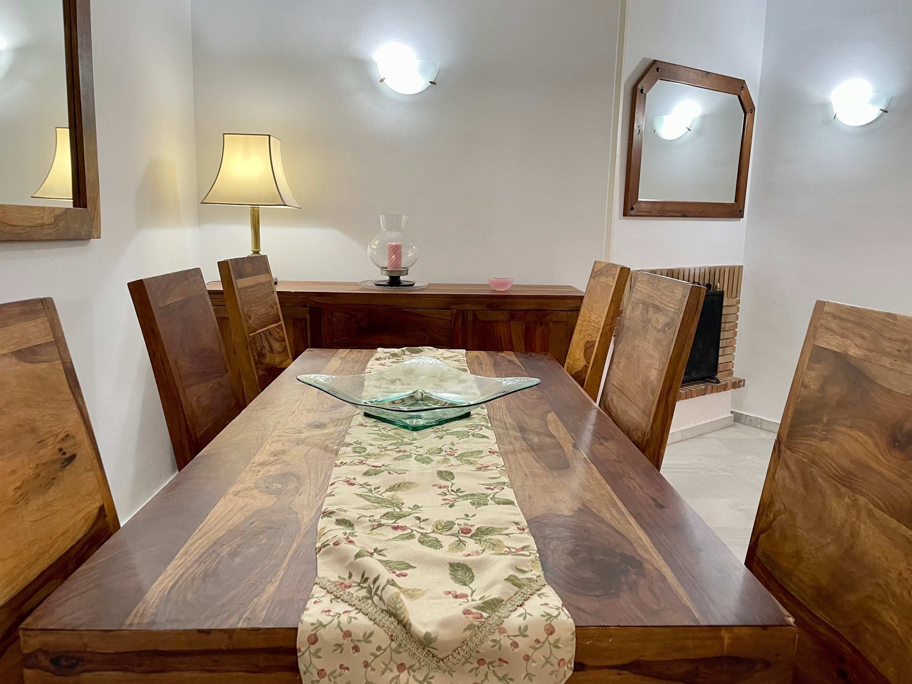 A dining table with a floral tablecloth, surrounded by wooden chairs.