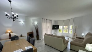 A modern living room with a sofa, a dining table, and a TV mounted on the wall. - Standard 2 Bedroom Ground Floor Apartment F-3 (Marbella)