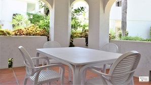 A patio with a white table and chairs, surrounded by white walls and arches, with greenery visible through the arches. - Standard 2 Bedroom Ground Floor Apartment F-3 (Marbella)