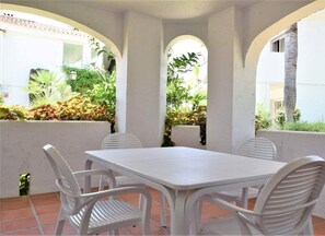 Une terrasse avec une table et des chaises blanches, entourée de murs et d’arcades blancs, et de laquelle on peut apercevoir la verdure à travers les arcades.