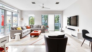 Ein modernes Wohnzimmer mit einem grauen Ecksofa, einem schwarzen Sessel und einem an der Wand montierten Flachbildfernseher.