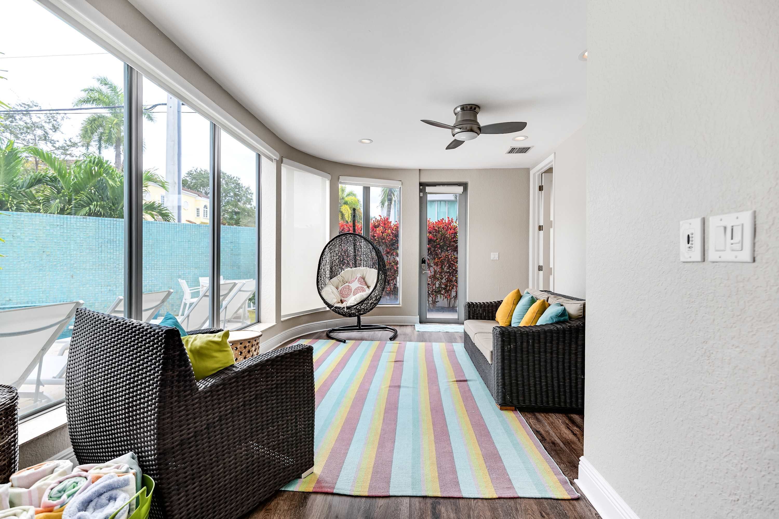 Ein modernes Wohnzimmer mit großen Fenstern, einem Deckenventilator und einem Streifenmuster-Teppich.