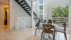 Ein geräumiges Zimmer mit moderner Wendeltreppe, einem Essbereich mit Stühlen und Tisch sowie großen Fenstern mit Blick auf Grünflächen.