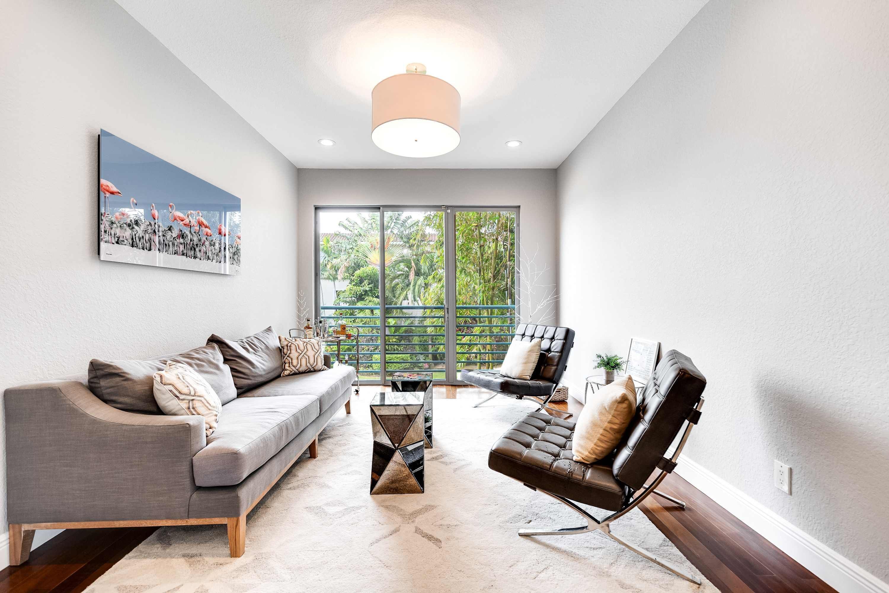 A modern living room with a grey sofa, a black leather chair, a coffee table, and a large window with a view of greenery.