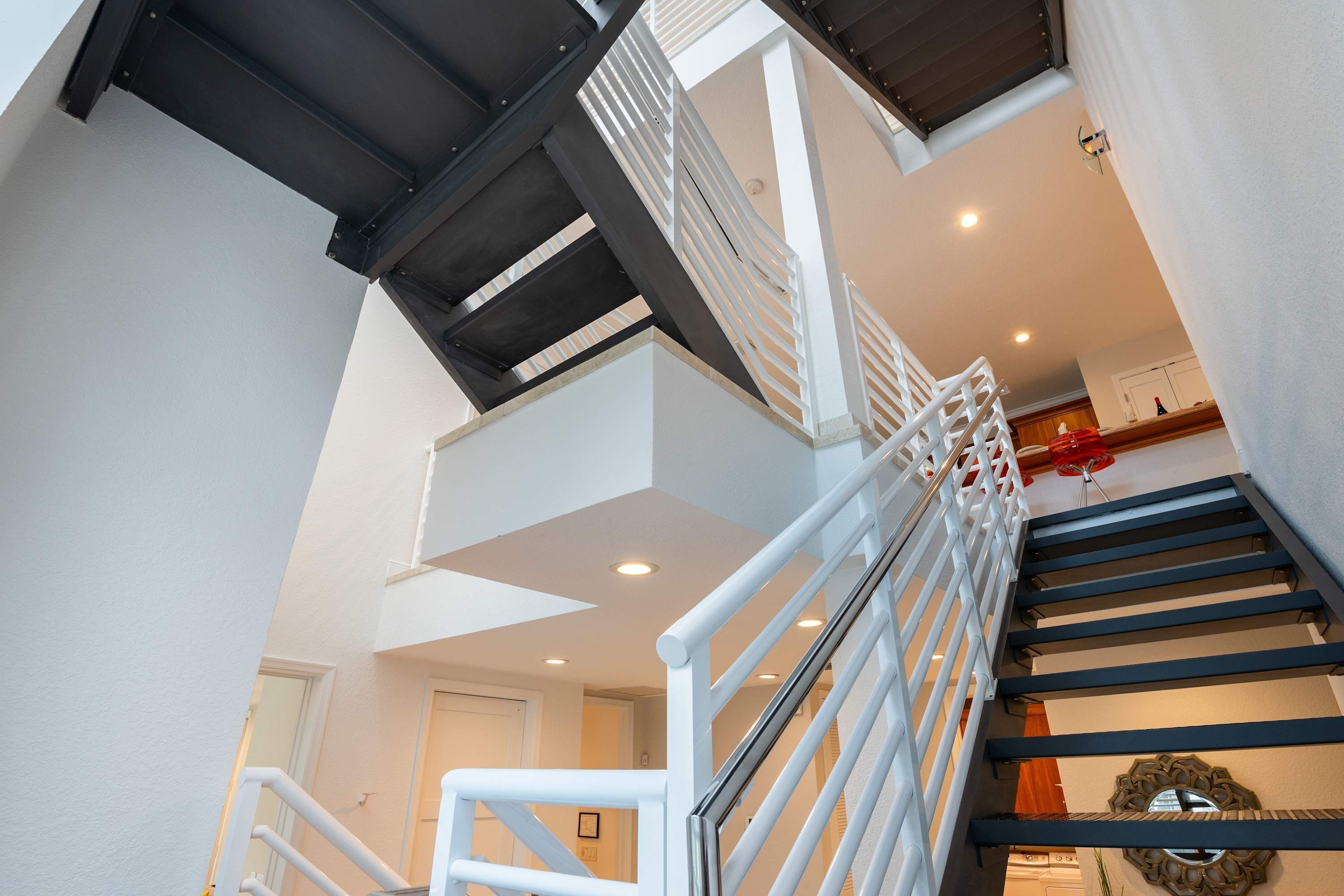 Eine Treppe mit weißen Geländern und dunklen Stufen, die zu einer zweiten Etage führt.