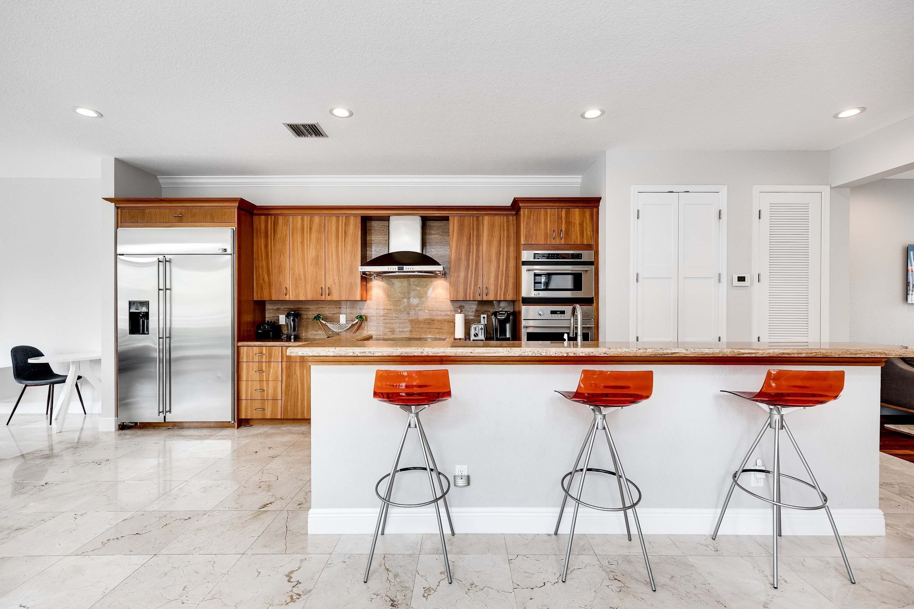 A modern kitchen with wooden cabinets, stainless steel appliances, and a marble floor.