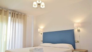 Habitación de hotel con cama, lámparas de noche, mesita de noche y ventana con cortinas.