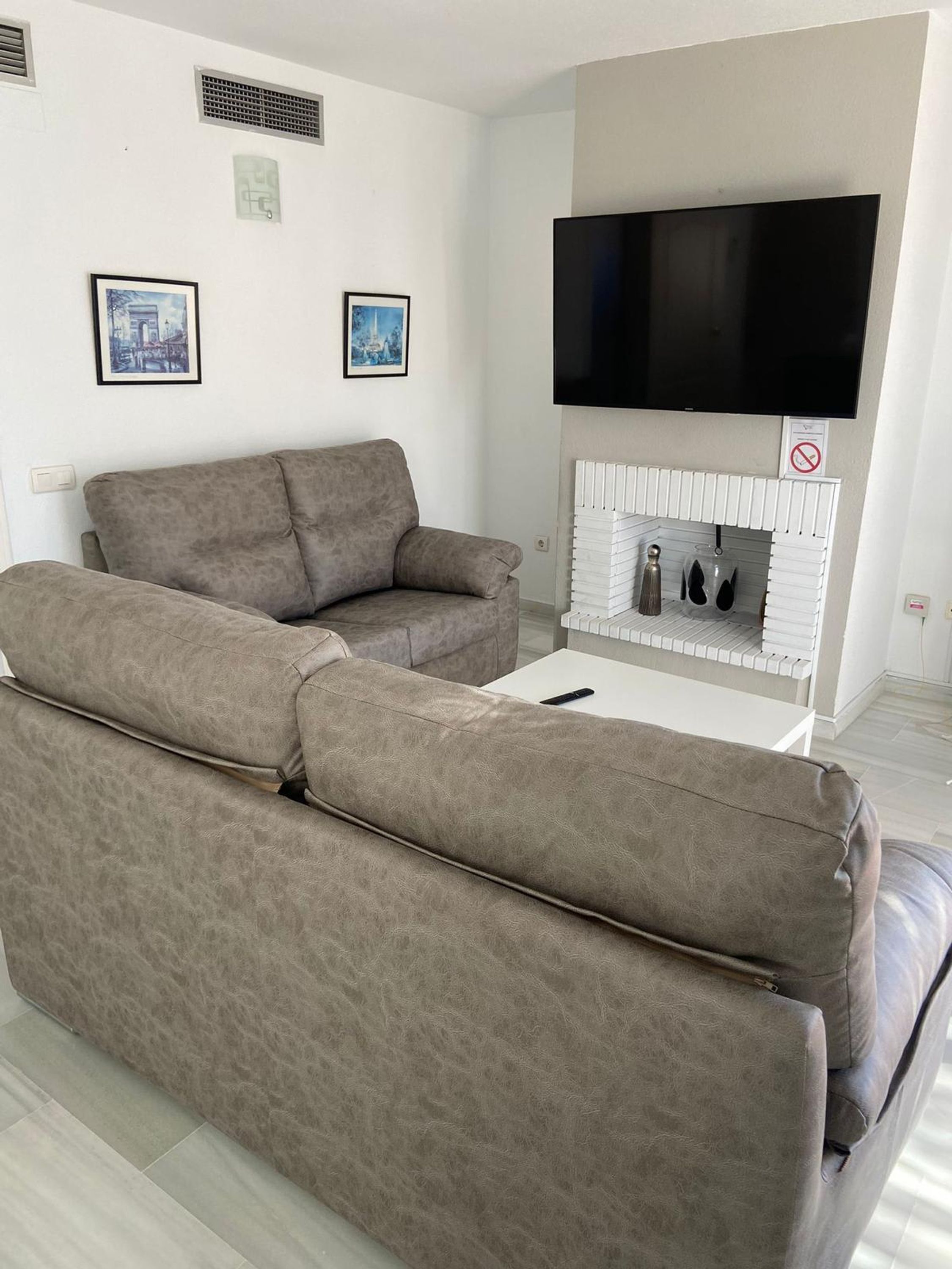 A living room with a large sectional sofa, a flat-screen TV mounted above a fireplace, and two framed pictures on the wall.