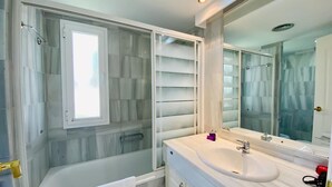 Une salle de bain moderne avec une douche à l’italienne en verre, une baignoire blanche et un meuble-lavabo doté d’un grand miroir.