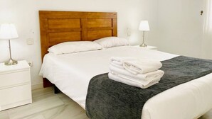 Un lit bien fait, avec des draps blancs, une tête de lit en bois et une pile de serviettes pliées posée au pied du lit.
