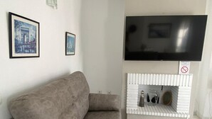 Un salon moderne avec un canapé gris, un téléviseur à écran plat fixé au-dessus d’une cheminée blanche, et deux tableaux encadrés accrochés au mur.