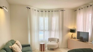 Una sala de estar con un sofá verde, un sillón blanco, una mesita con una lámpara y un televisor.