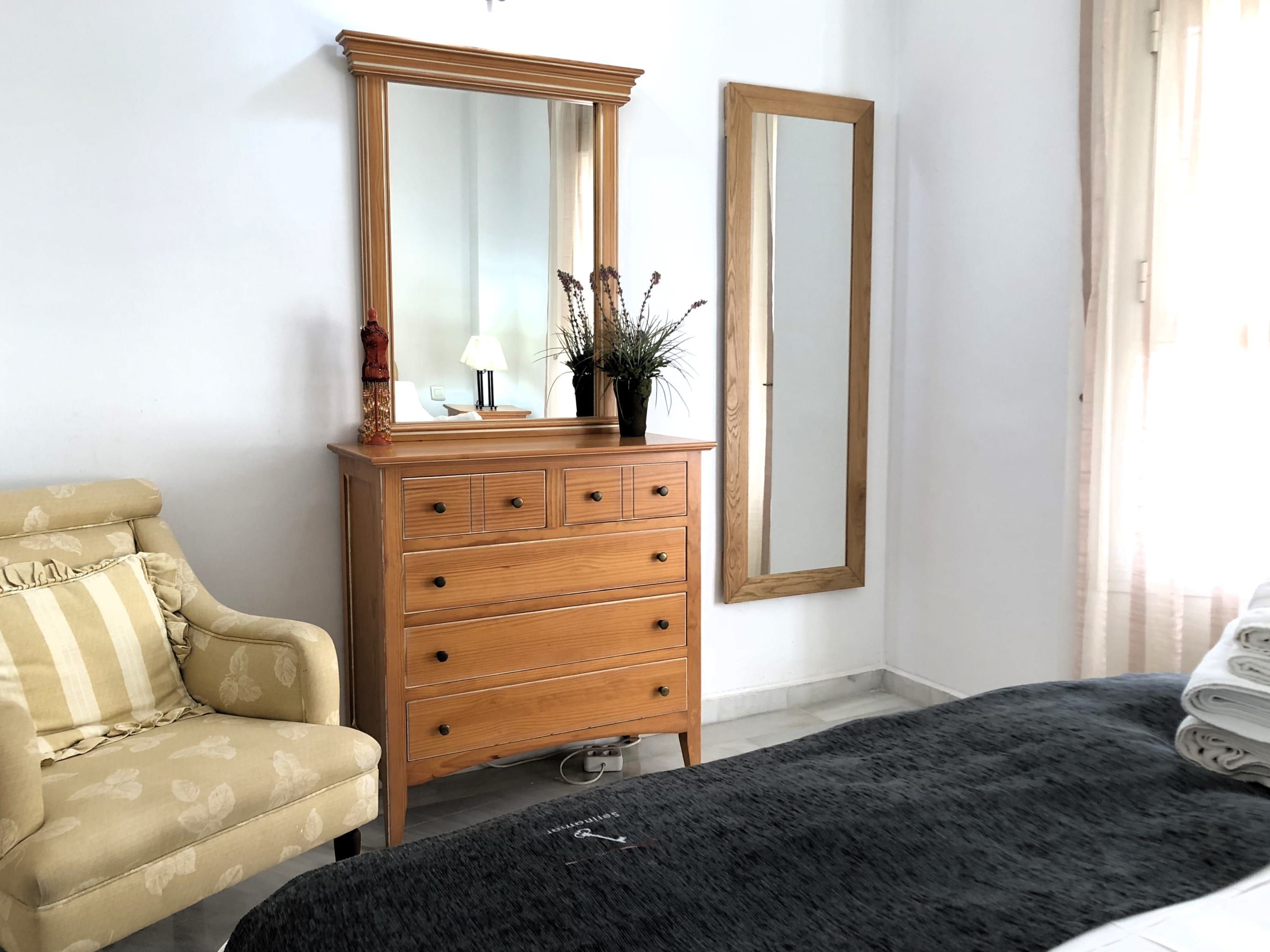 Une chambre à coucher avec une commode en bois, un miroir, un canapé et un lit recouvert d’une couverture foncée.