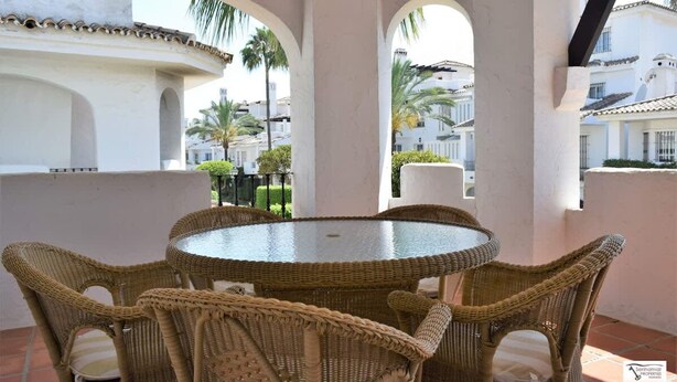 A wicker table and chairs set on a balcony with a view of palm trees and buildings. - Bright 2 Bedroom First Floor F-4 (Marbella)