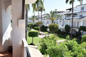 A courtyard with neatly trimmed hedges, palm trees, and a view of white buildings with balconies. - Bright 2 Bedroom First Floor F-4 (Marbella)