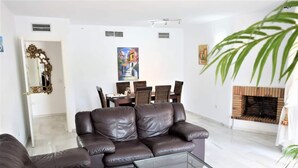A living room with a brown leather sofa, a glass coffee table, a dining area with a painting, and a fireplace. - Bright 2 Bedroom First Floor F-4 (Marbella)