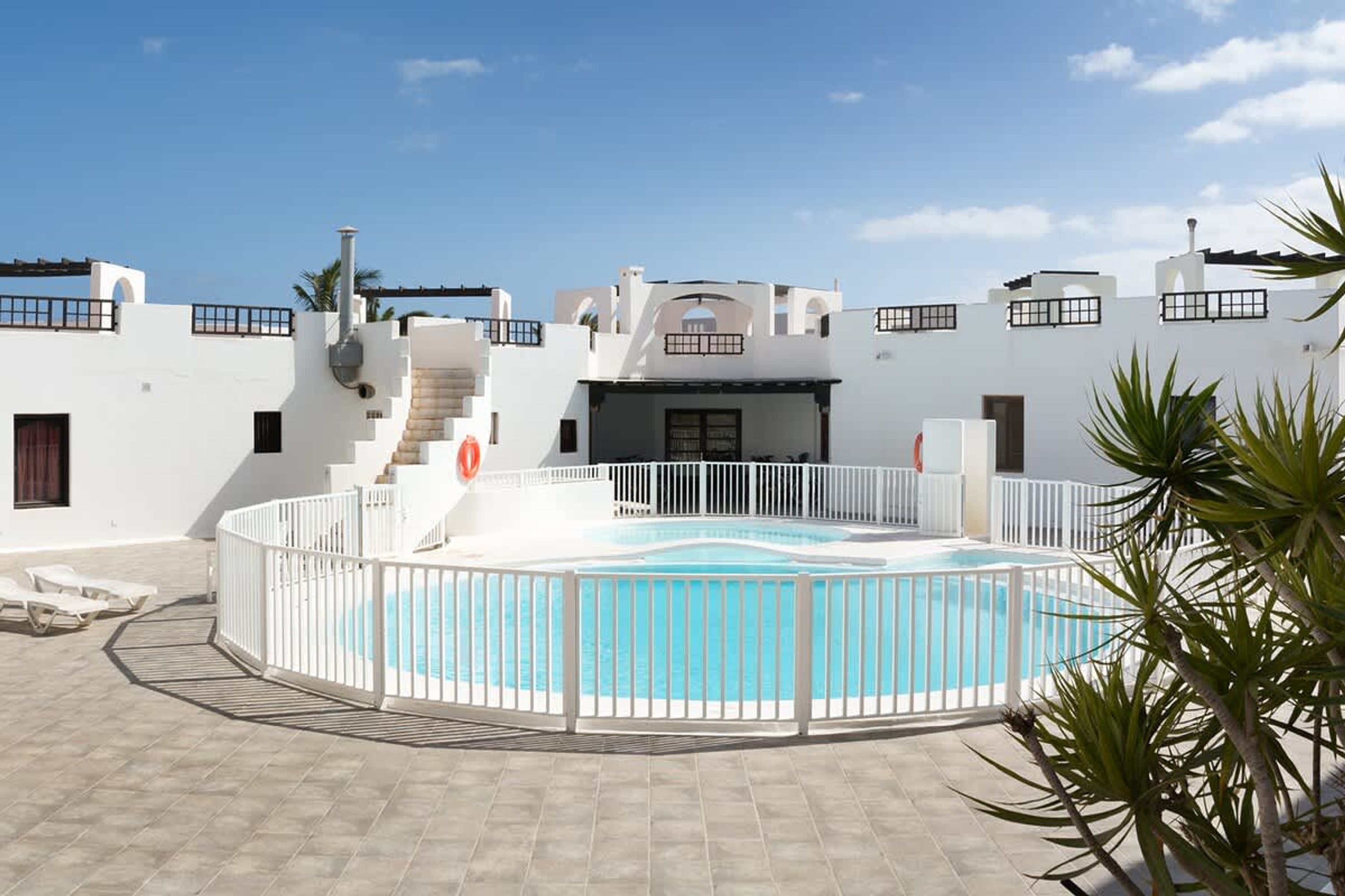 A pool area with a white fence, a staircase leading to a covered area, and a clear blue sky.