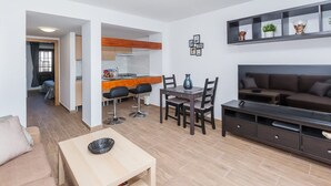 Un apartamento moderno con comedor, sofá, mueble para televisor y cocina al fondo.