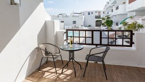 Un balcón con dos sillas y una mesa, con vista a un complejo de edificios blancos con balcones.