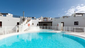 Una piscina con zona de borde blanca, una escalera que lleva a un edificio y un cielo azul despejado.