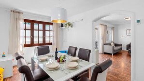 A dining area with a table set for four, surrounded by chairs, with a hanging light fixture above.
