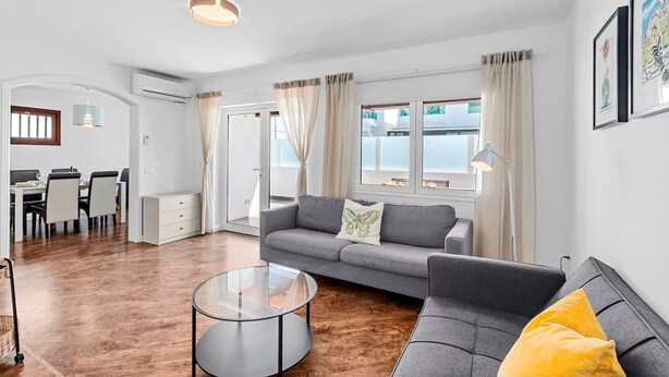 A modern living room with a grey sofa, a round coffee table, and a dining area with a white table and chairs.