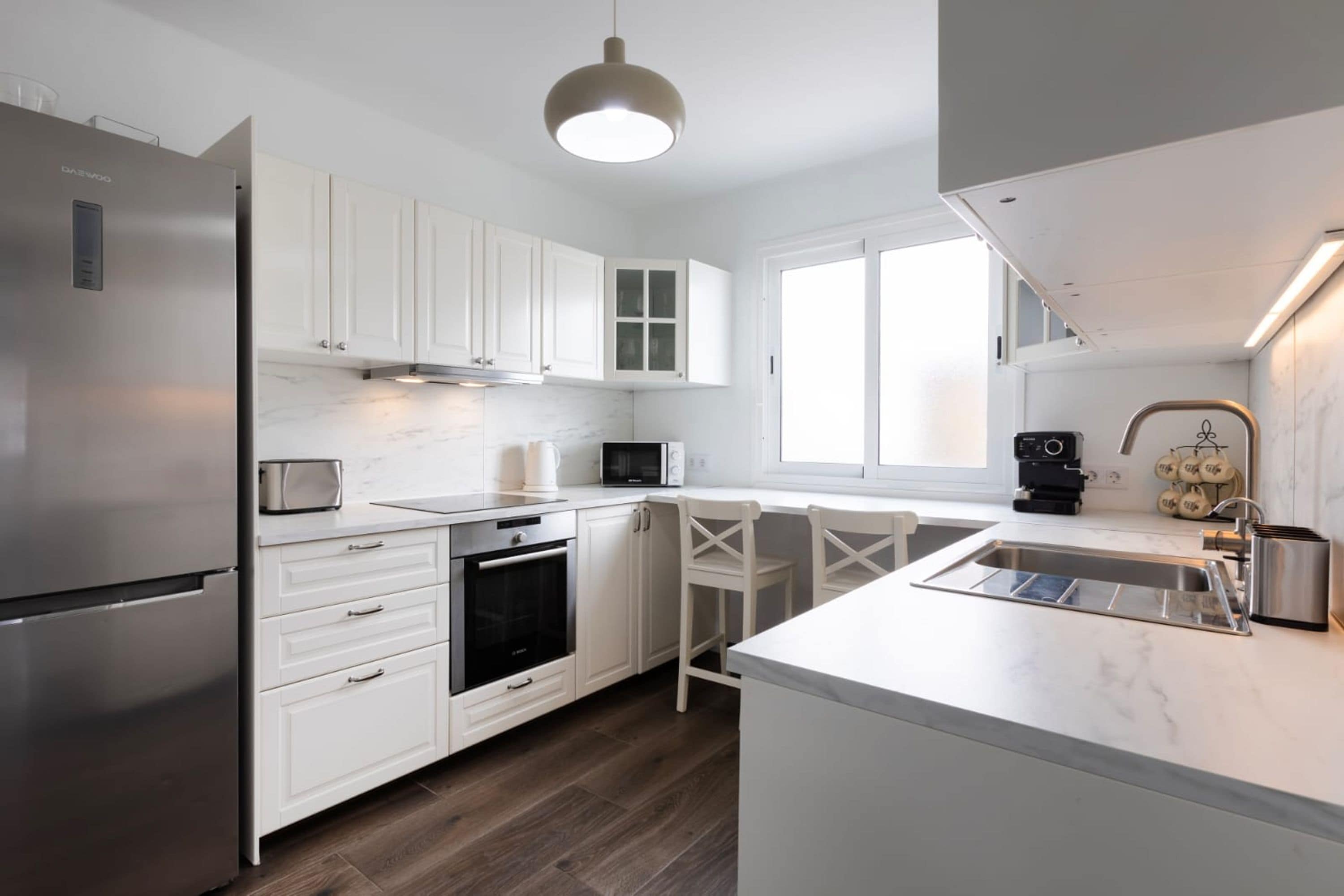 A modern kitchen with white cabinetry, a stainless steel refrigerator, a built-in oven, and a microwave.