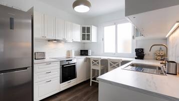 A modern kitchen with white cabinetry, a stainless steel refrigerator, a built-in oven, and a microwave.