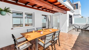 A dining area with a wooden table and chairs, a balcony with chairs, and a hanging plant.