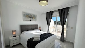 A modern bedroom with a large bed, a nightstand, a lamp, a painting, and a view of the outdoors. - Exceptional Views - Dama de Noche 1 Bedroom Penthouse (Marbella)