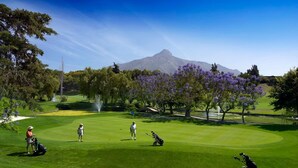 A golf course with a mountain in the background, trees, and a clear sky. - Exceptional Views - Dama de Noche 1 Bedroom Penthouse (Marbella)