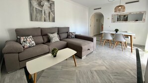 A modern living room with a sectional sofa, a dining table with chairs, and a minimalist design. - Exceptional Views - Dama de Noche 1 Bedroom Penthouse (Marbella)