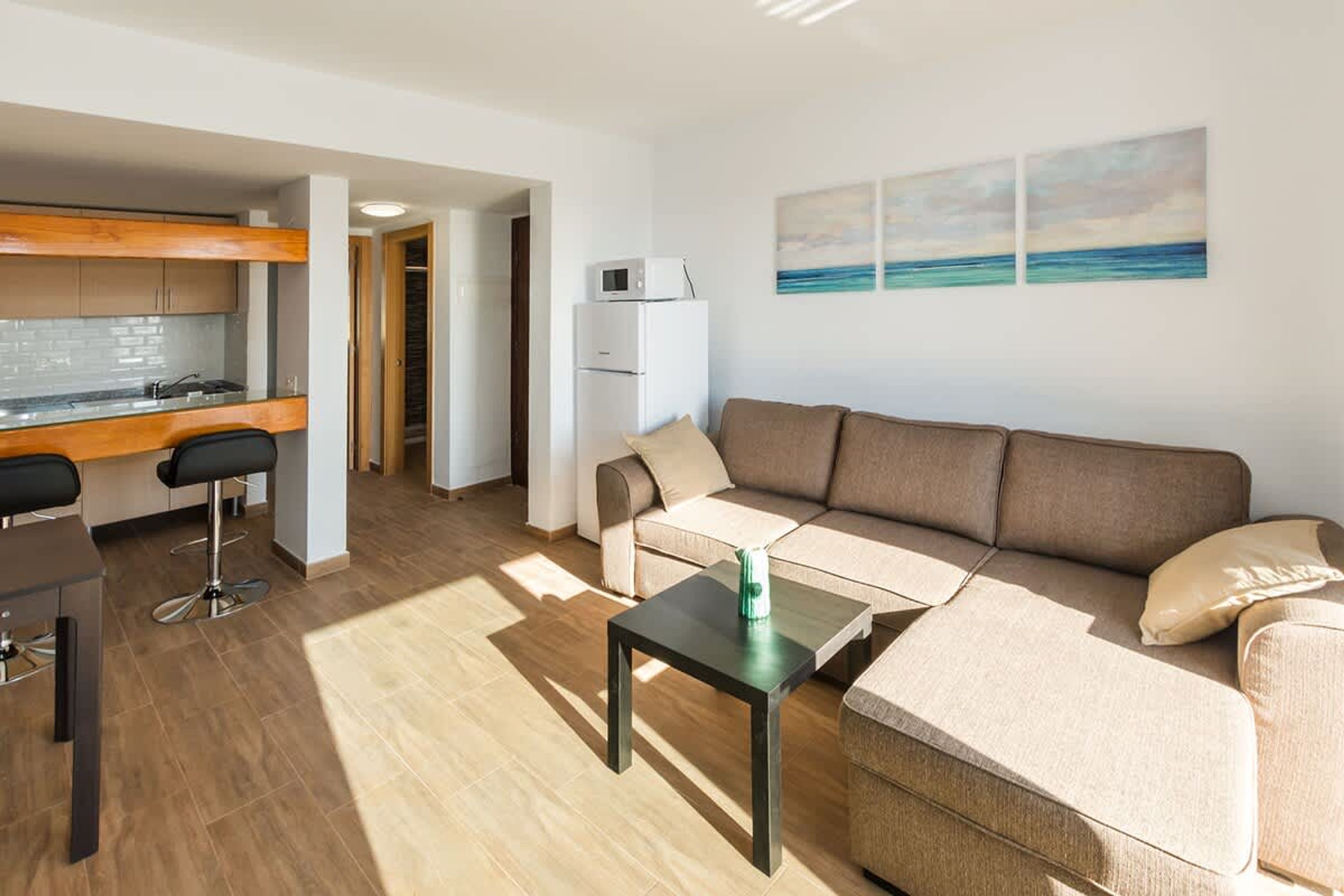 A modern living room with a sofa, a coffee table, and a kitchen area with a refrigerator and a microwave.