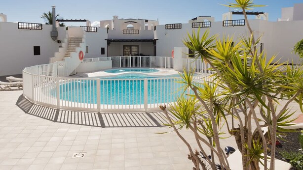 A pool area with a hot tub, surrounded by a white fence and palm trees. - Apartamento Golden Teguise 2 (Alcorcon)