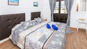 A bedroom with a large bed, a nightstand, a window with curtains, and two framed pictures on the wall. - Apartamento Golden Teguise 2 (Alcorcon)