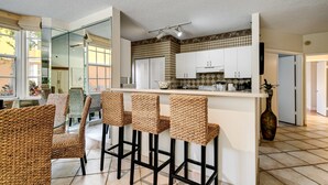 Una cocina moderna con armarios blancos, una isla central con taburetes y un ventanal con vistas a la calle.