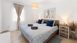 Een slaapkamer met een bed, nachtkastjes, een hanglamp en een schilderij aan de muur.