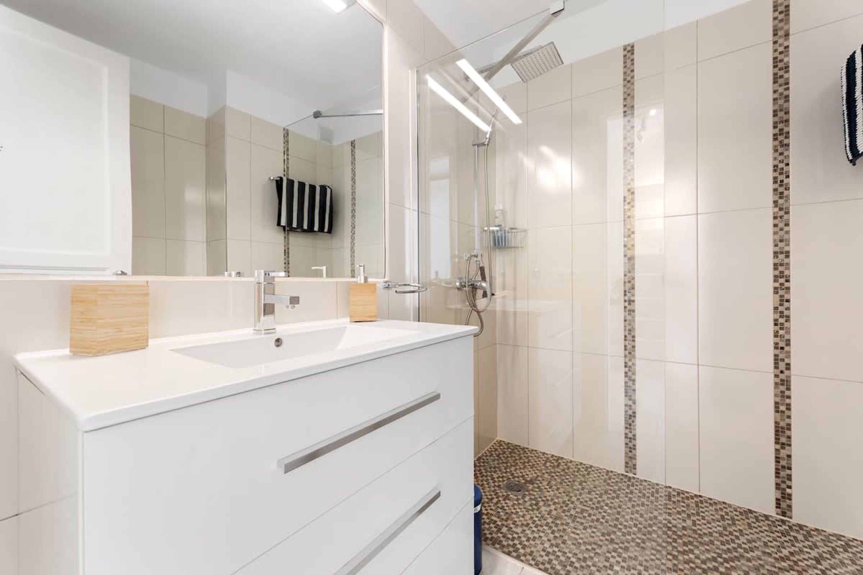 Un baño moderno con tocador blanco, un espejo grande y una zona de ducha.