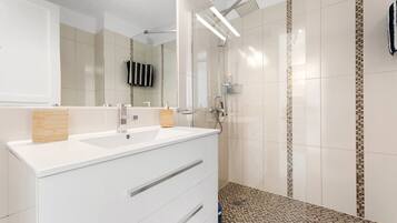 Un baño moderno con tocador blanco, un espejo grande y una zona de ducha.