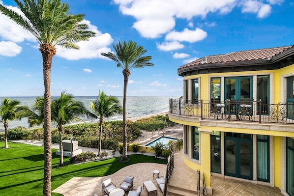 A two-story house with a balcony overlooking the ocean, a swimming pool, and a well-maintained lawn.
