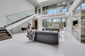 Un espace de vie spacieux et moderne, avec un grand canapé gris, un escalier doté de rampes en verre et une cheminée.