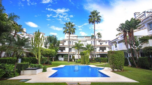 Una piscina rodeada de abundante vegetación y un edificio de varios pisos con balcones.