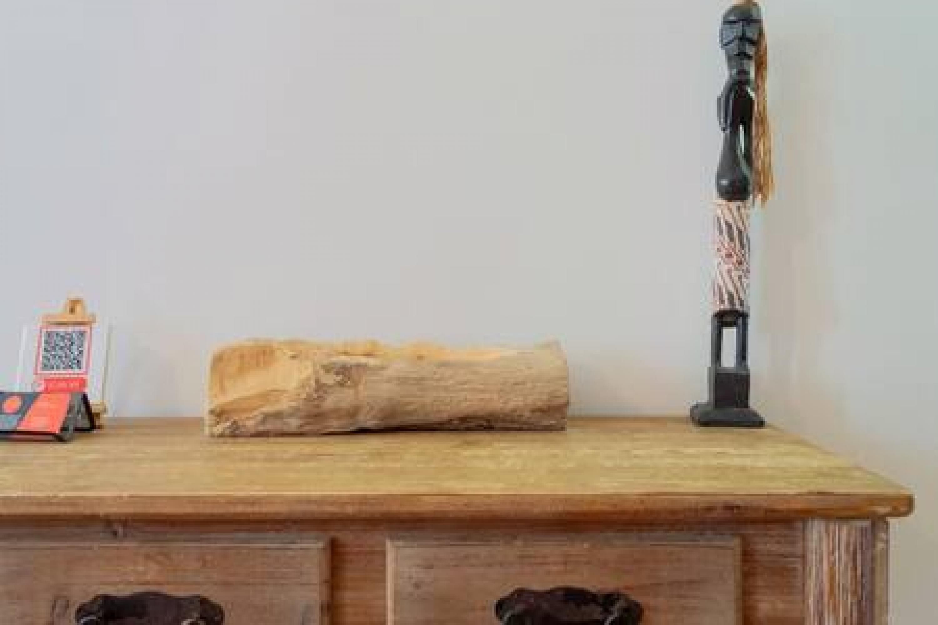 A wooden dresser with drawers, a decorative wooden piece, a small statue, and a QR code.