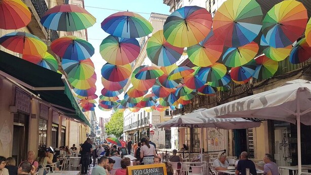 Calle con mesas al aire libre, sombrillas de colores y una pizarra anunciando una oferta especial.