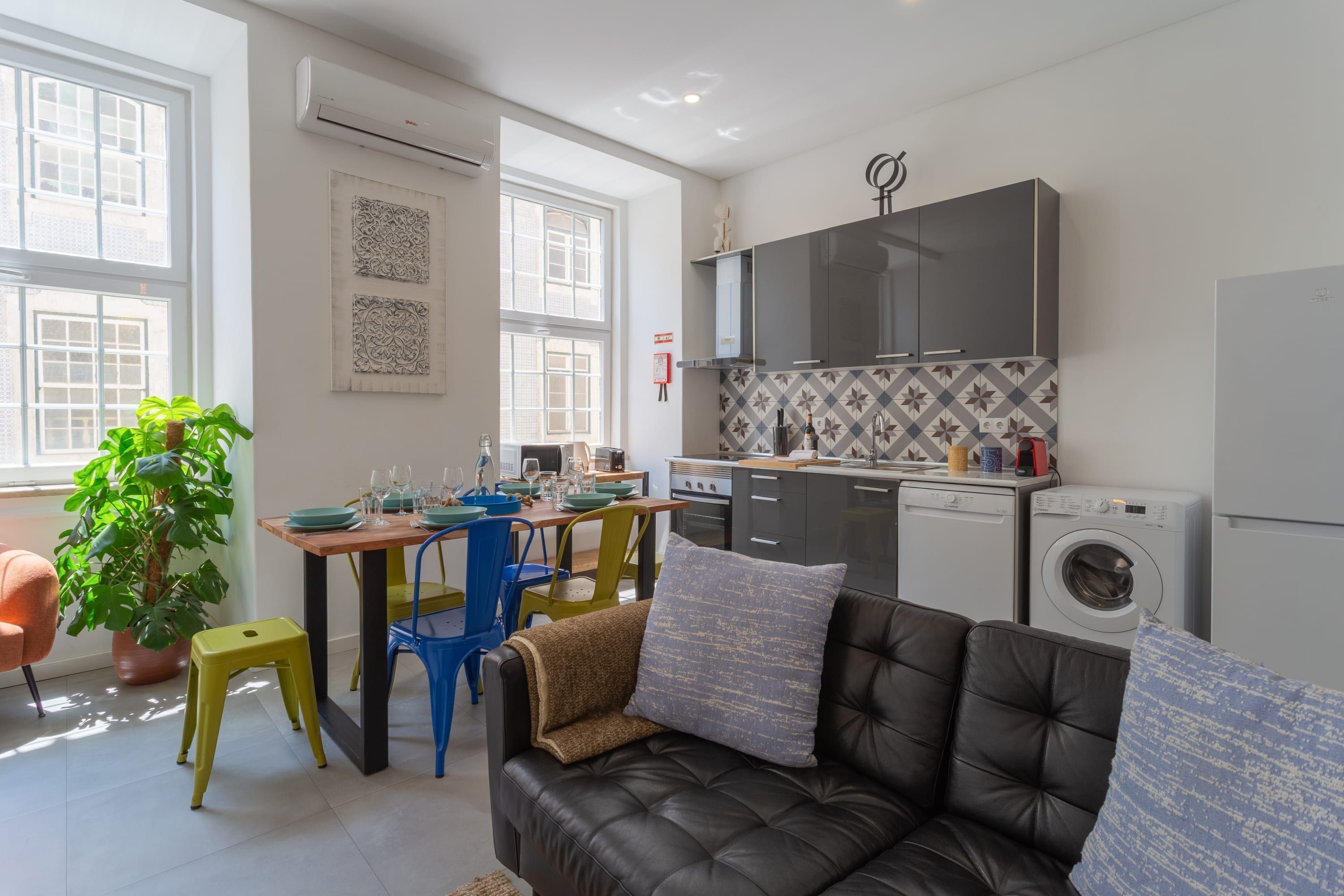 Un espace de vie compact comprenant un coin repas, un canapé, un lave-linge et une cuisine équipée d’appareils électroménagers modernes.